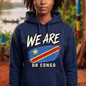 May include: A navy blue hooded sweatshirt featuring the text WE ARE in white, a graphic of the Democratic Republic of the Congo flag with a yellow star, and the text DR CONGO in white. The hoodie includes a front kangaroo pocket and long sleeves.