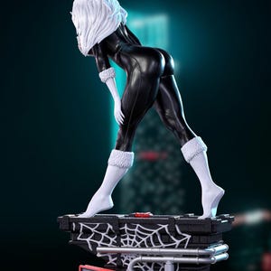 May include: A statue of a character in a black catsuit with white fur trim and white hair. The figure is posed on a brick-like base with a spiderweb design. The statue has a dynamic pose and is set against a dark background.