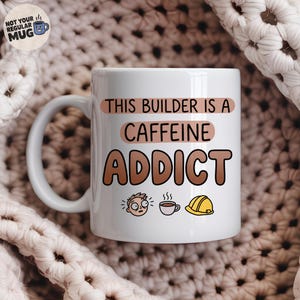 Könnte beinhalten: Ein weißer Keramikbecher mit dem Text THIS BUILDER IS A CAFFEINE ADDICT in brauner und pfirsichfarbener Schrift. Unter dem Text befinden sich drei kleine Illustrationen: ein Gesicht mit weit aufgerissenen Augen, eine dampfende Kaffeetasse und ein gelber Bauhelm.