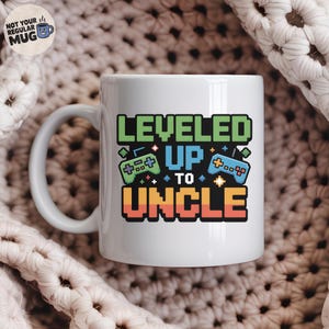 Könnte beinhalten: Weiße Keramik-Tasse mit dem Text "LEVELED UP TO UNCLE" in pixeligen grünen, blauen und orangefarbenen Buchstaben. Die Tasse zeigt zwei pixelige Gamecontroller-Grafiken. Die Tasse hat einen weißen Henkel und die Worte "NOT YOUR REGULAR MUG" an der Seite.