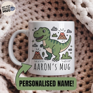 Op de afbeelding: Witte keramische mok met een groene cartoon dinosaurus. De mok heeft de tekst "Aaron's Mug" en "Personalised Name!" en illustraties van wolken, vulkanen en bomen. De mok heeft een wit handvat.