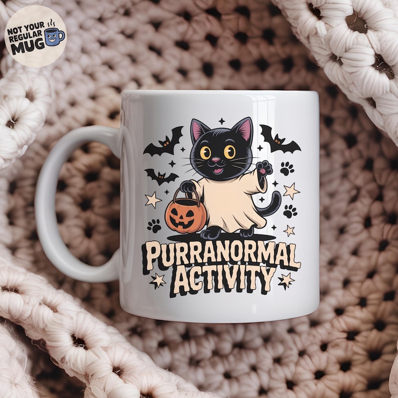 May include: White ceramic mug featuring a black cat dressed as a ghost, holding a jack-o'-lantern. The mug has the text "PURRANORMAL ACTIVITY" with bats, paw prints, and stars. The mug has a curved handle and the text "NOT YOUR REGULAR MUG".