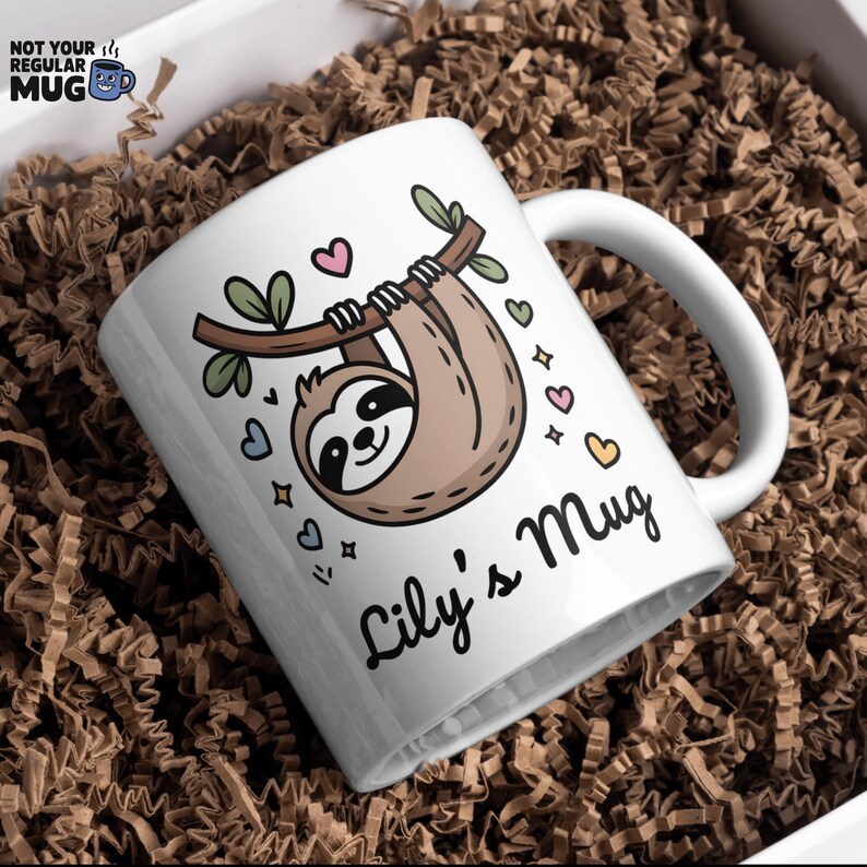 May include: White ceramic mug featuring a cartoon sloth hanging from a branch, surrounded by hearts and stars. The mug has the text "Lily's Mug" in a script font. The top left corner has the text "NOT YOUR REGULAR MUG".