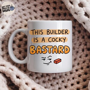 May include: A white ceramic mug featuring the black and orange text THIS BUILDER IS A COCKY BASTARD. Below the text is a simple black line drawing of a smirking face and a small red brick. The mug has a curved handle on the left side.