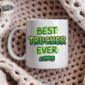 May include: A white ceramic mug featuring the green text BEST TRUCKER EVER printed over light green brush stroke accents. Below the text is a small, simple illustration of a green semi-truck. The mug has a standard handle on the left side.