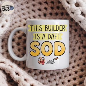 May include: A white ceramic mug featuring the black text THIS BUILDER IS A DAFT SOD with yellow highlights behind the words. Below the text is a cartoon face with a tongue sticking out and a small grey trowel with a brown handle.