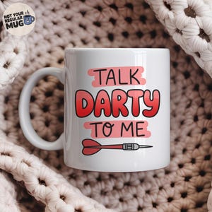Può includere: Una tazza in ceramica bianca con il testo TALK DARTY TO ME in lettere rosse e rosa. La parola DARTY è in un grande carattere rosso, mentre TALK e TO ME sono in nero su sfondi rettangolari rosa. Una freccetta rossa è illustrata sotto il testo.