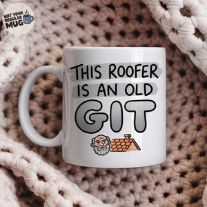 Puede incluir: Una taza de cerámica blanca con el texto en negro "THIS ROOFER IS AN OLD GIT" sobre un fondo gris. Debajo del texto hay una pequeña ilustración de dibujos animados de un hombre mayor con barba junto a un tejado de color marrón.