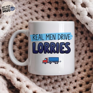 May include: A white ceramic mug featuring the text "REAL MEN DRIVE LORRIES" in dark blue letters with a light blue highlight behind the first line. Below the text is a small graphic of a red and blue semi-truck with a trailer and exhaust smoke.