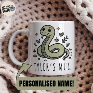 Może przedstawiać: Biały ceramiczny kubek z kreskówkowym wzorem węża w odcieniach zieleni, z napisem "Tyler's Mug" i "Personalised Name!". Kubek ma biały uchwyt i jest ozdobiony liśćmi i gwiazdami.