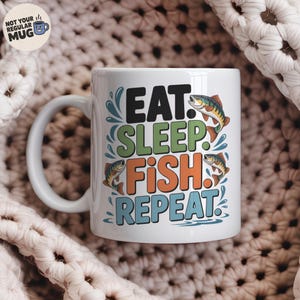 Puede incluir: Taza de cerámica blanca con el texto "EAT. SLEEP. FISH. REPEAT." en negro, verde, naranja y azul. La taza presenta ilustraciones de peces y salpicaduras de agua. La taza tiene un asa blanca y las palabras "NOT YOUR REGULAR MUG" están en la parte superior izquierda.