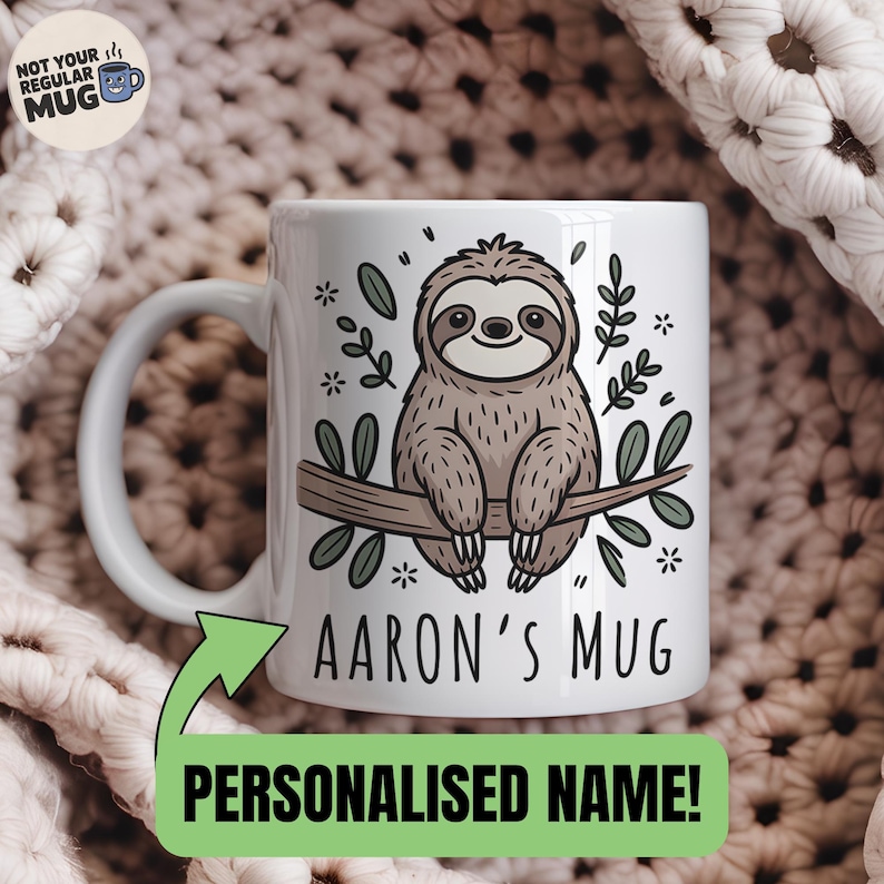 K&ouml;nnte beinhalten: Wei&szlig;e Keramiktasse mit einem Cartoon-Faultier auf einem Ast, umgeben von gr&uuml;nen Bl&auml;ttern und Sternen. Die Tasse zeigt "Aaron's Mug" und "Personalised Name!". Au&szlig;erdem ist der Text "NOT YOUR REGULAR MUG" aufgedruckt.