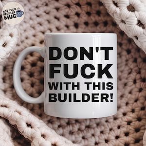 Könnte beinhalten: Ein weißer Keramikbecher mit dem schwarzen Text DON'T FUCK WITH THIS BUILDER!, der in einer fetten, serifenlosen Schrift auf der Vorderseite aufgedruckt ist. Der Becher hat einen Standardhenkel auf der linken Seite und eine glatte, glänzende Oberfläche.