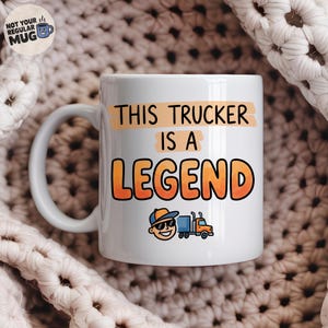 May include: A white ceramic mug featuring the black text THIS TRUCKER IS A and the large orange text LEGEND. Below the text is a colorful graphic of a smiling person wearing a blue cap and sunglasses next to a small orange and blue semi-truck.