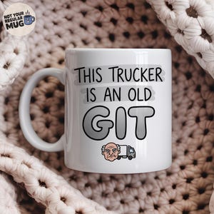 Puede incluir: Una taza de cerámica blanca con el texto en negro THIS TRUCKER IS AN OLD GIT, una ilustración de una persona gruñona y un camión gris. La taza tiene un asa en el lado izquierdo y un logotipo circular en la esquina superior izquierda.