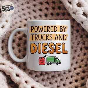 Peut inclure: Un mug en céramique blanc avec le texte noir "POWERED BY TRUCKS AND" sur des fonds rectangulaires jaunes, et le mot "DIESEL" en grandes lettres orange en dessous. Un petit graphique d'un bidon d'essence rouge souriant et d'un camion vert.
