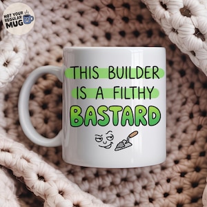 May include: A white ceramic mug featuring the green text THIS BUILDER IS A FILTHY BASTARD, accompanied by a small cartoon face and a trowel icon. The mug has a handle on the left side and is positioned against a textured, cream-coloured knit fabric.