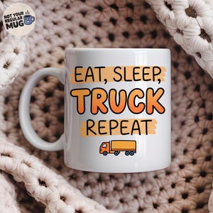 May include: A white ceramic mug featuring the black text EAT, SLEEP, REPEAT with the word TRUCK in large orange letters. Below the text is a small orange semi-truck graphic. A circular logo in the top left corner reads NOT YOUR REGULAR MUG.
