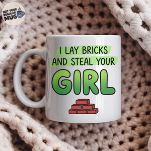 Könnte beinhalten: Ein weißer Keramikbecher mit dem Text I LAY BRICKS AND STEAL YOUR GIRL in grüner Schrift und einer kleinen Abbildung einer roten Ziegelmauer darunter. Ein kreisförmiges Logo oben links zeigt NOT YOUR REGULAR MUG mit einem blauen Bechersymbol.