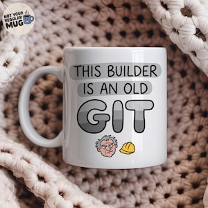 May include: A white ceramic mug featuring the black text THIS BUILDER IS AN OLD GIT. The design includes a small illustration of a grumpy-looking person with grey hair and a yellow hard hat positioned below the text on the front of the mug.