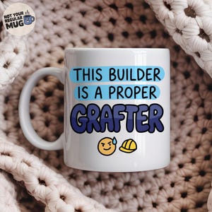 Op de afbeelding: Een witte keramische mok met de tekst THIS BUILDER IS A PROPER GRAFTER in blauwe en donkerblauwe letters. Onder de tekst staat een geel emoji-gezichtje met een zweetdruppel en een geel icoon van een veiligheidshelm. De mok heeft een oor links.
