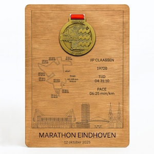 Op de afbeelding: Houten plaquette ter herdenking van de Marathon Eindhoven. Voorzien van een gouden medaille met de tekst "Marathon Eindhoven" en een routekaart. Bevat details van de loper, tijd en tempo. De tekst "12 oktober 2025" is ook zichtbaar.
