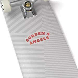 May include: A skateboard deck with a gray and white striped pattern. The deck features the text "CORDEN'S ANGELS" in red letters. The skateboard has silver trucks and white wheels.