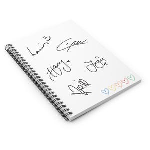 May include: A white spiral-bound notebook featuring multiple black signatures. The notebook has a row of colorful hearts along the bottom edge. The signatures are written in black ink.
