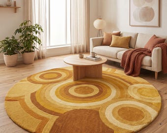 Puede incluir: Una alfombra redonda grande con un patrón texturizado de círculos concéntricos en varios tonos de amarillo, dorado y naranja quemado. La alfombra tiene un pelo grueso y afelpado y está colocada sobre un suelo de madera clara en una sala.