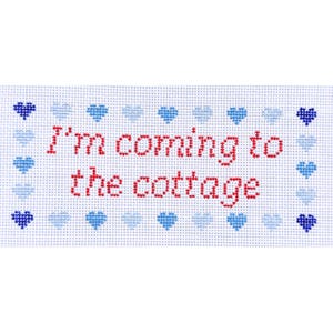 May include: A cross-stitched rectangular piece with the words "I'm coming to the cottage" in red. The text is centered on a white background, framed by a border of blue hearts.