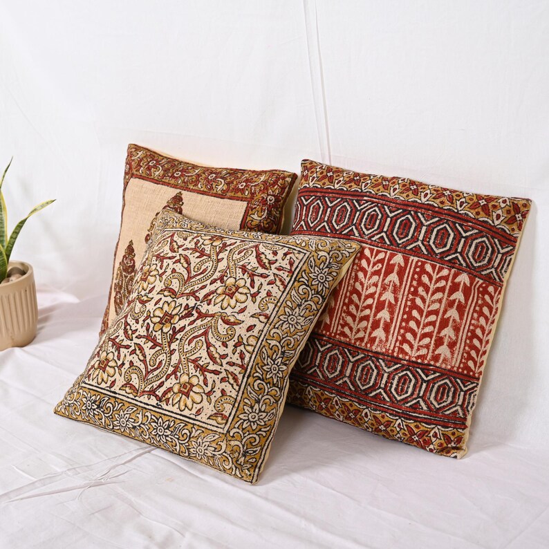 May include: Three decorative throw pillows with intricate floral and geometric patterns in shades of red, beige, and gold. The pillows are square-shaped and appear to be made of a textured fabric, adding a touch of warmth and style to any living space.