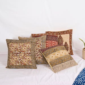 May include: A collection of five decorative throw pillows with floral and geometric patterns. The pillows feature a color palette of cream, red, and gold. The designs include floral motifs, geometric borders, and stylized patterns, creating a bohemian aesthetic.