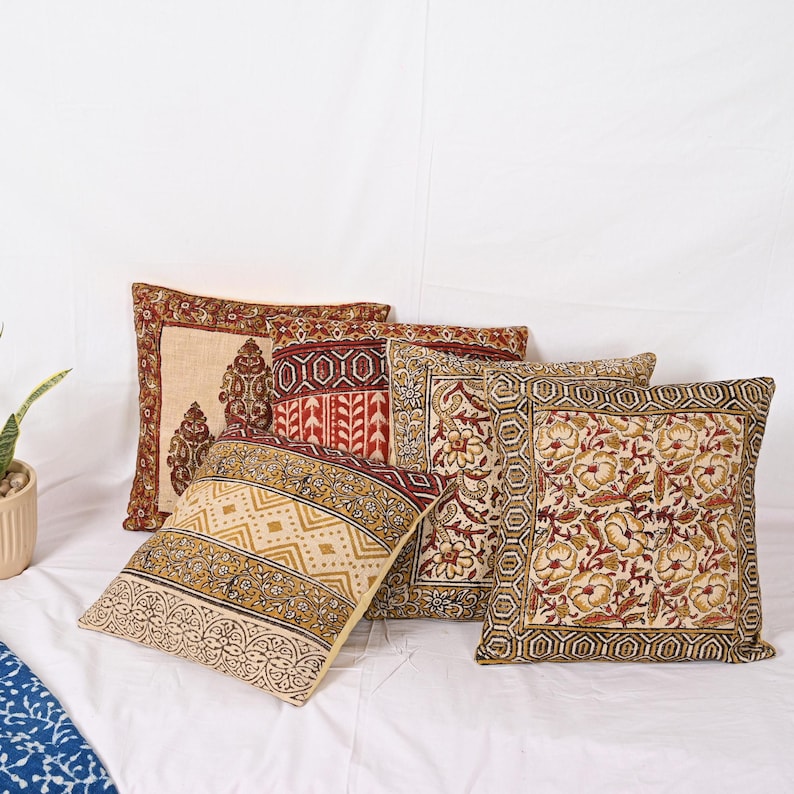 May include: Five square decorative throw pillows with various patterns. The pillows feature floral, geometric, and paisley designs in shades of beige, red, and gold. The pillows are arranged on a white surface.