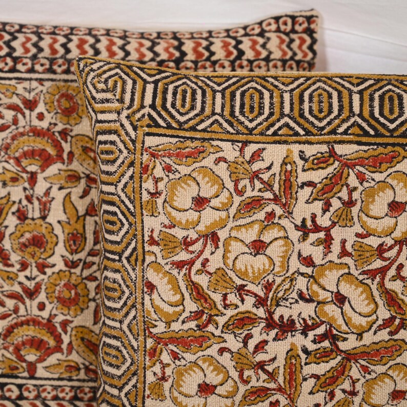 May include: Two decorative throw pillows with a floral pattern. The pillows feature a cream-colored background with a repeating pattern of yellow and red flowers and leaves. The borders are black and gold with geometric designs.