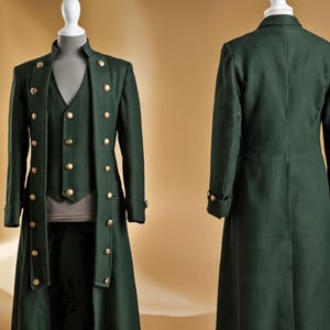 May include: A dark green, three-piece suit displayed on a mannequin. The suit includes a long coat with gold buttons, a vest, and matching pants. The coat has a high collar and long sleeves. The vest has gold buttons. The suit is made of a textured fabric.