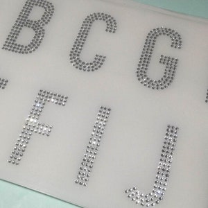 May include: A set of silver rhinestone letters, A through J, on a white background.