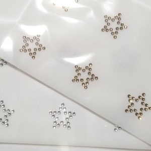 May include: Two sheets of clear plastic with silver and gold star-shaped rhinestones. The rhinestones are arranged in a star shape.