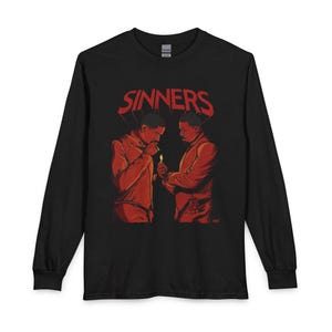 May include: A black long-sleeve t-shirt featuring a red graphic print of two individuals lighting a cigarette. The word SINNERS is printed in large red letters above the figures. The design uses red and orange tones against the black fabric.