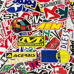 May include: A vibrant assortment of stickers, showcasing a variety of logos and designs. Brands such as Mechanix Wear, Acerbis, and Bilstein are visible, alongside racing-themed graphics and text. The stickers are in different shapes and sizes.