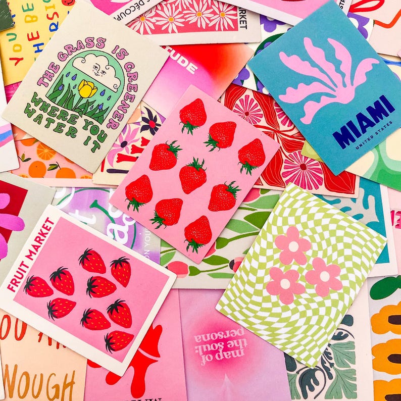 May include: A collection of colorful cards with various designs. Some cards feature strawberries, flowers, and the text "FRUIT MARKET." Others display the text "MIAMI UNITED STATES" and phrases like "The grass is greener where you water it."