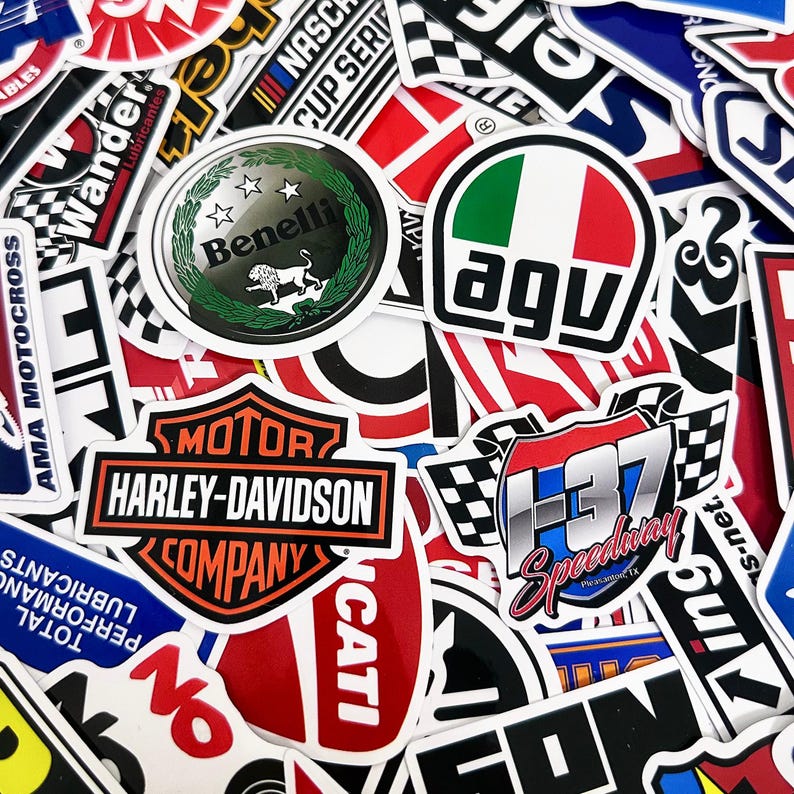 May include: A collection of colorful stickers featuring various logos and designs. Prominent stickers include the Harley-Davidson logo, a Benelli emblem, and an AGV logo with the Italian flag colors. Other stickers display racing and automotive themes.
