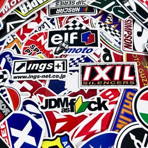 Puede incluir: Una colección de pegatinas coloridas con varios logotipos y texto. Las pegatinas presentan marcas como "ELF moto", "IXIL SILENCERS" y "JDM as fck". Las pegatinas son de varias formas y tamaños, con una mezcla de temas de carreras y automoción.