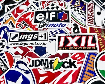 Pode incluir: Uma coleção de autocolantes coloridos com vários logótipos e texto. Os autocolantes apresentam marcas como "ELF moto", "IXIL SILENCERS" e "JDM as fck". Os autocolantes são de várias formas e tamanhos, com uma mistura de temas de corrida e automóveis.