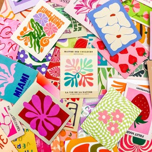 May include: A collection of colorful art prints with various designs. Some prints feature floral patterns, strawberries, and the text "Miami" and "Rions danser". The prints are in shades of pink, blue, green, and orange.