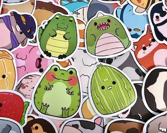 May include: A collection of colorful, cartoon animal stickers. The stickers include a green alligator, a green dinosaur, a green frog, and a green watermelon. Other stickers feature a fox, a penguin, and a cow.