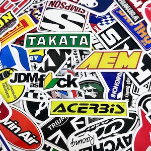 May include: A collection of colorful stickers with various logos and text. The stickers feature brands like TAKATA, AEM, and ACERBIS, with a mix of shapes and designs. The stickers are arranged closely together.