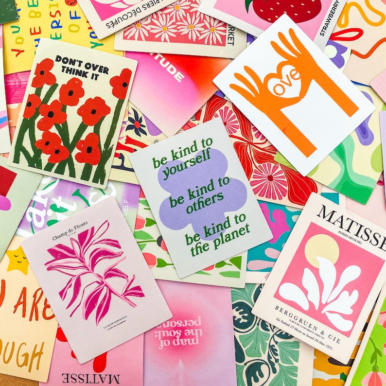 May include: A collection of colorful cards with various designs and text. Some cards feature floral illustrations, while others display phrases like "Don't Over Think It" and "Be kind to yourself." The cards are scattered, creating a vibrant and artistic display.