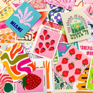 May include: A collection of colorful art prints and cards with various designs. Some cards feature strawberries, the text "FRUIT MARKET", and the text "MIAMI UNITED STATES". Other cards have floral and abstract patterns.