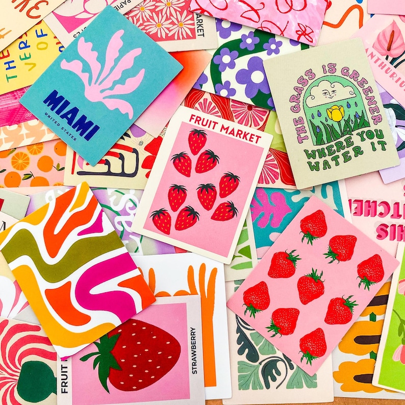 May include: A collection of colorful art prints and cards with various designs. Some cards feature strawberries, the text "FRUIT MARKET", and the text "MIAMI UNITED STATES". Other cards have floral and abstract patterns.