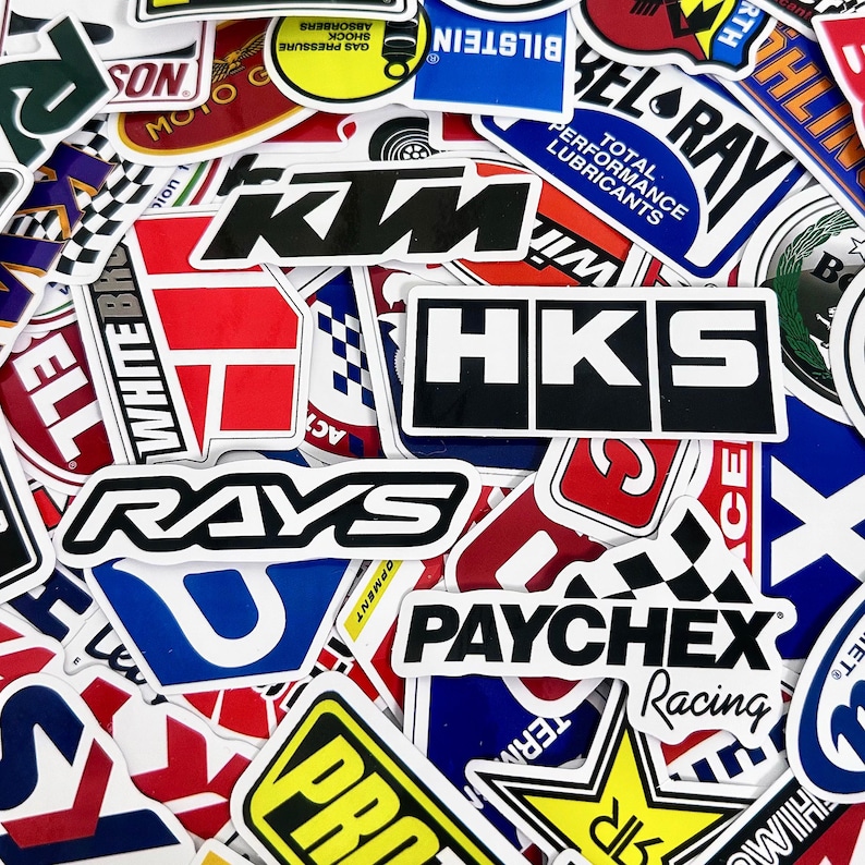 May include: A collection of colorful stickers with various logos and text. The stickers feature brands like HKS, RAYS, and PAYCHEX Racing. The stickers are in various shapes and sizes, with a mix of bold colors and fonts.